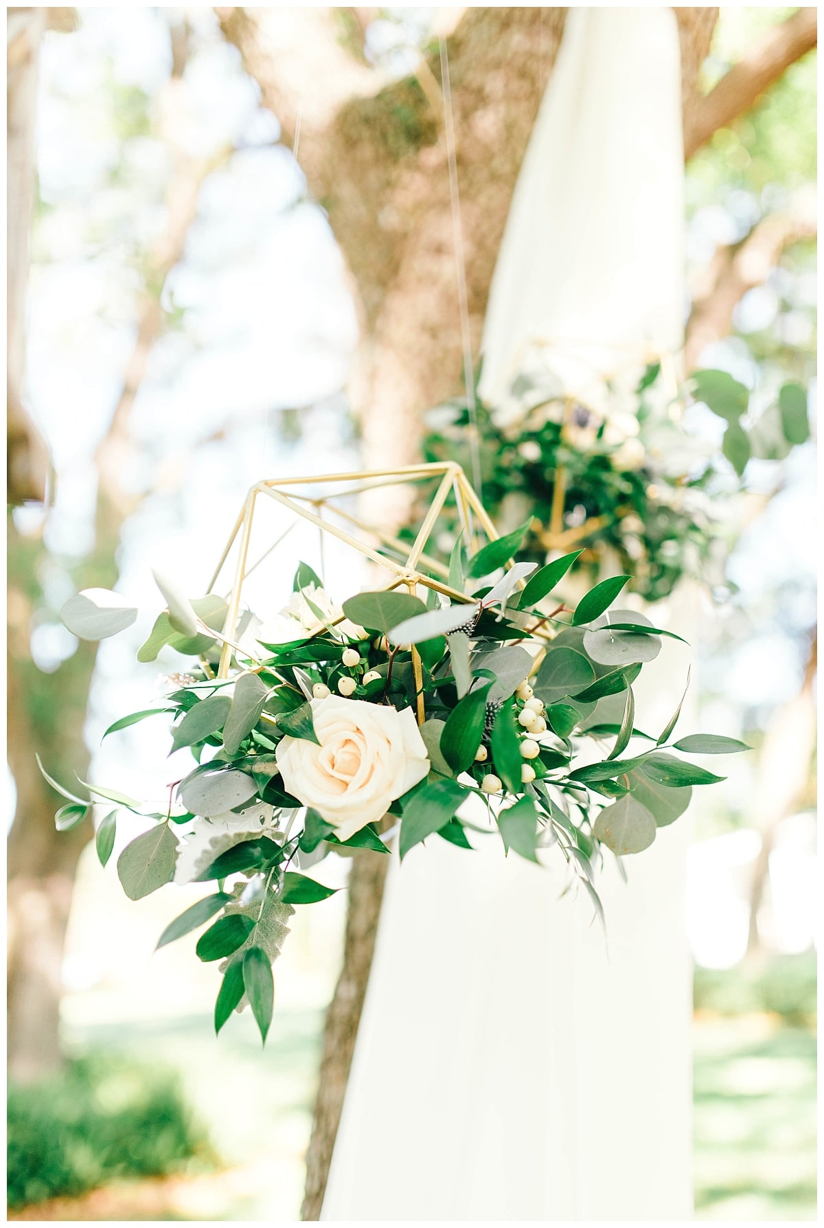 Hanging gold geo's filled with fresh greenery and garden roses hung from simple ivory drapery
