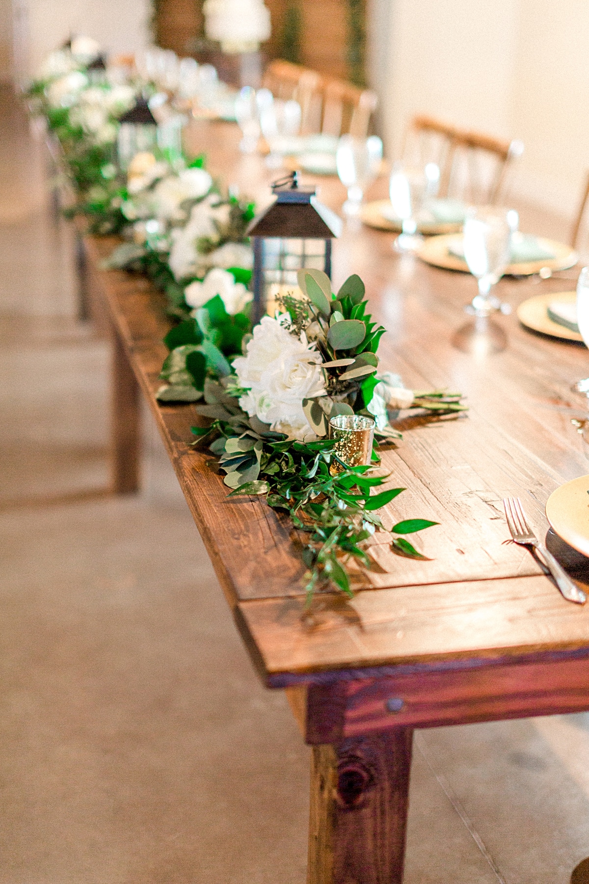rustic reception farm table with greenery runners and vintage lanterns