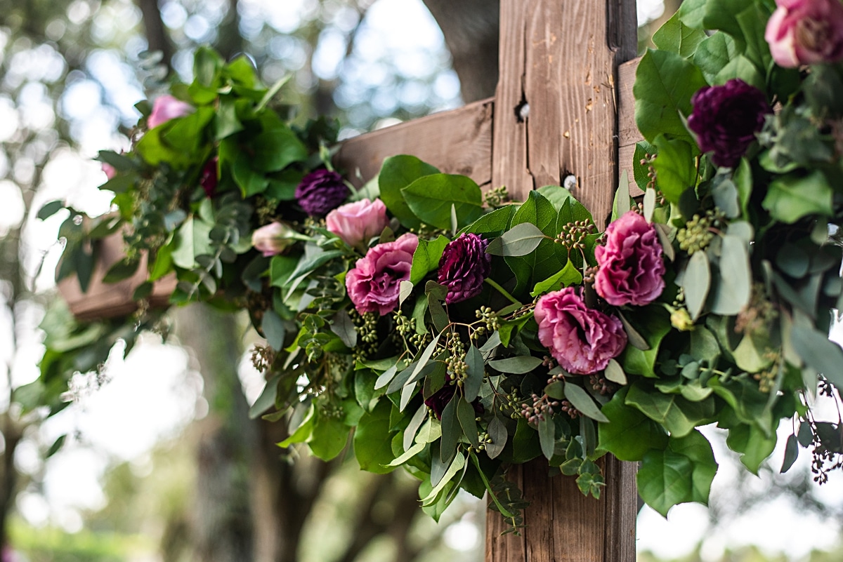 Jewel toned florals in various shades of blush with greenery decorating traditional wooden cross arbor