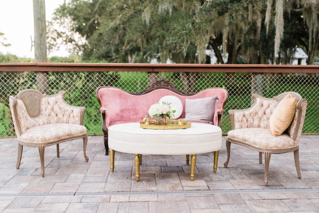 Vintage regency style lounge set featuring pink velvet sofa and floral side chairs with cream ottoman