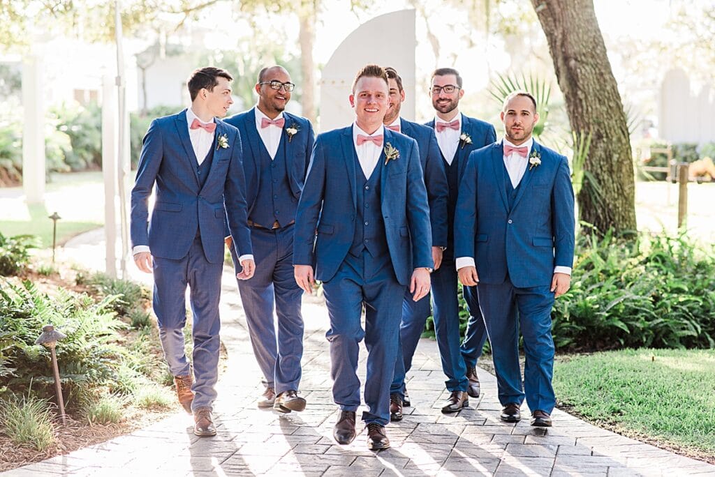 Groom and groomsmen matching blue three piece suits with pink bow ties