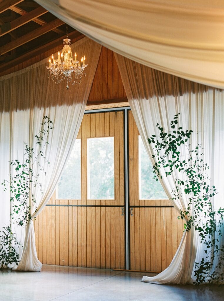 rustic sliding barn doors open up to natural light, wood rafters and vintage crystal chandeliers in this florida barn venue