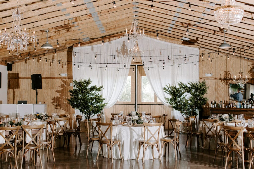 rustic barn wedding reception with string lights, vintage crystal chandeliers and indoor trees 